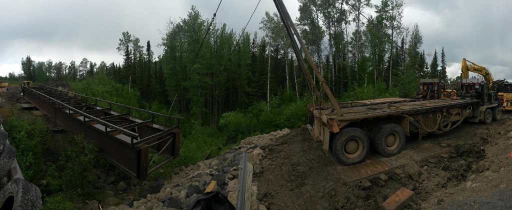 steel bridge in forest being moved by large excavator